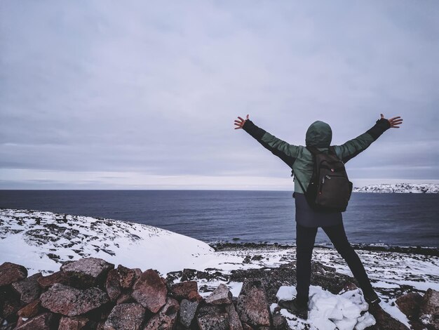 L'hiver, l'homme au-dessus de la falaise rocheuse lève les bras face à l'horizon de la mer, concept de liberté. voyageur au bord de la terre. L'océan Arctique.