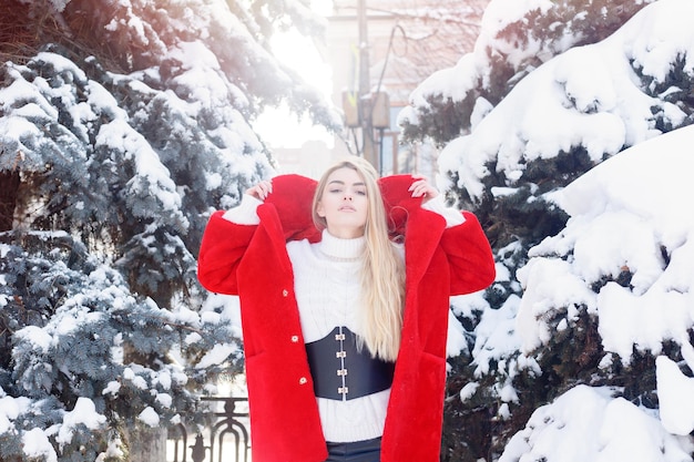 Hiver, mode, concept de personnes - mode Portrait d'une belle jeune femme se promène dans la ville souriante manteau de fourrure rouge gros plan flocons de neige hiver froid, respire l'air frais au jour de gelée d'hiver. le coucher du soleil