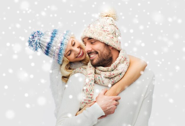 hiver, mode, couple, noël et concept de personnes - homme et femme souriants en chapeaux et écharpe étreignant sur fond de neige