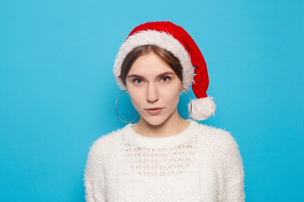 Hiver, noël, gens, concept de beauté - jolie blonde portant un chapeau de noël sur fond bleu clair. Portrait de jeune belle jolie fille joyeuse souriante regardant la caméra sur fond blanc.