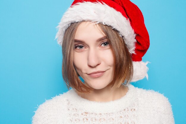 Hiver, Noël, gens, concept de beauté - jolie blonde portant un chapeau de Noël sur une surface bleu clair