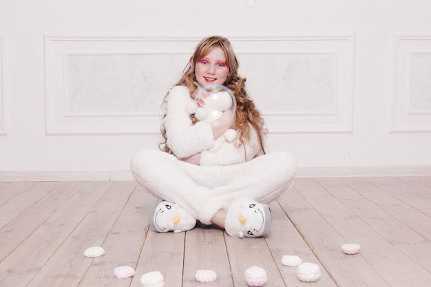 Hiver, Noël, vacances, bonbons, anniversaire, célébration et concept d'enfants - Pyjama mignon de petite fille avec des bonbons assis sur le sol, concept d'enfance heureuse. cadeaux de fille, chien doux, bulles de savon.