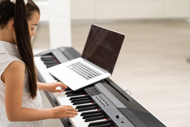 Homeschool petite jeune fille apprenant le piano à partir d'un ordinateur se connectant à un cours de musique en ligne sur Internet par un enseignant. Nouveau mode de vie normal et éducation, concept d'étude des étudiants à la maison.