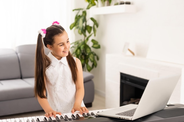Homeschool petite jeune fille apprenant le piano à partir d'un ordinateur se connectant à un cours de musique en ligne sur Internet par un enseignant. Nouveau mode de vie normal et éducation, concept d'étude des étudiants à la maison.
