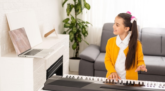 Homeschool petite jeune fille apprenant le piano à partir d'un ordinateur se connectant à un cours de musique en ligne sur Internet par un enseignant. Nouveau mode de vie normal et éducation, concept d'étude des étudiants à la maison.