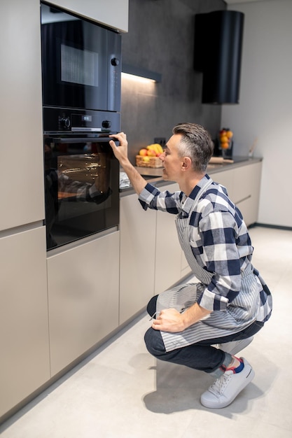 Homme accroupi près du four touchant la poignée