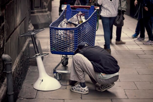 Photo un homme accroupi sur le trottoir d'un chariot d'achat en ville