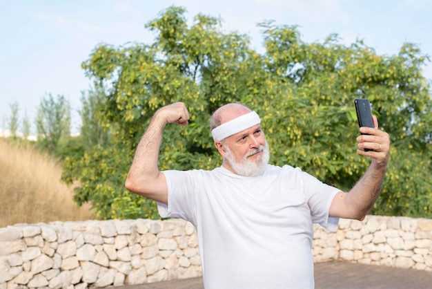 Un homme actif mature dans le parc prend un selfie avec son smartphone tout en exhibant ses biceps