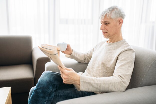 Homme adulte assis sur un canapé et lisant le journal