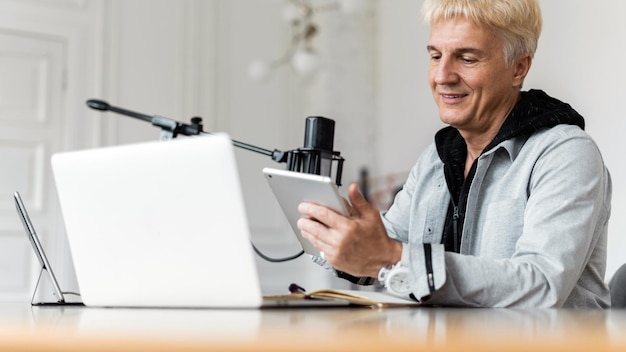 Un homme adulte aux cheveux gris travaillant sur le blogueur radio utilise un ordinateur portable et un microphone