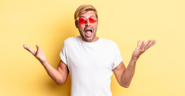 Homme adulte blond se sentant heureux et étonné de quelque chose d'incroyable et portant des lunettes de soleil