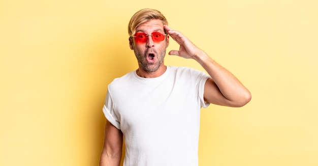 Homme adulte blond semblant heureux, étonné et surpris et portant des lunettes de soleil