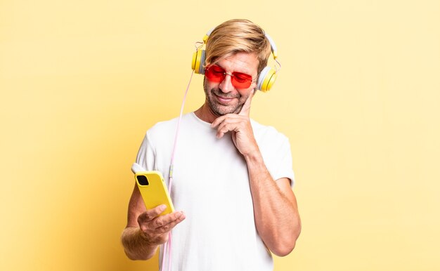 Homme adulte blond souriant joyeusement et rêvant ou doutant avec des écouteurs