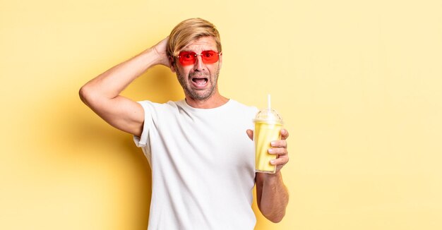 Homme adulte blond stressé, anxieux ou effrayé, les mains sur la tête avec un milk-shake