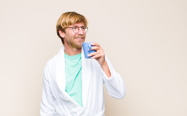 Homme adulte blonde portant un peignoir et des lunettes et tenant une tasse de café
