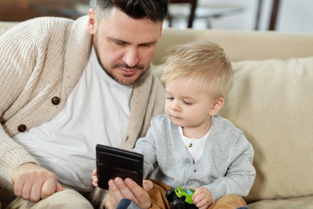 Homme adulte avec charmant petit fils assis sur le canapé en regardant gadget ensemble