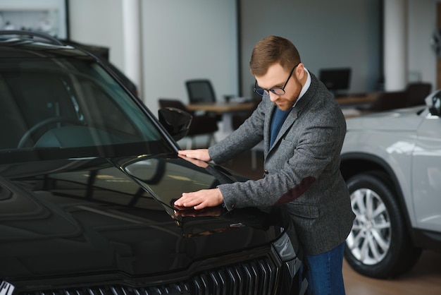 Homme adulte client acheteur masculin porte un costume classique chemise blanche choisit l'auto veut acheter une nouvelle voiture de contrôle tactile automobile dans la salle d'exposition salon de véhicule concessionnaire magasin salon de l'automobile concept de vente intérieur