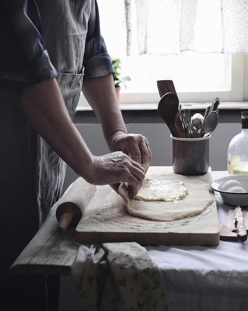 homme adulte cuisiner des aliments pétrir la pâte sur la table sur fond intérieur de cuisine rustique