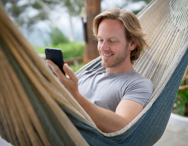 Un homme adulte dans un hamac utilisant un téléphone intelligent pour naviguer sur Internet pendant les vacances d'été