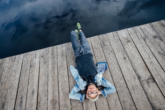 Photo homme adulte élégant se trouvant sur le vieux quai en bois au-delà du lac. rêve de hipster barbu heureux en lunettes portrait d'en haut.