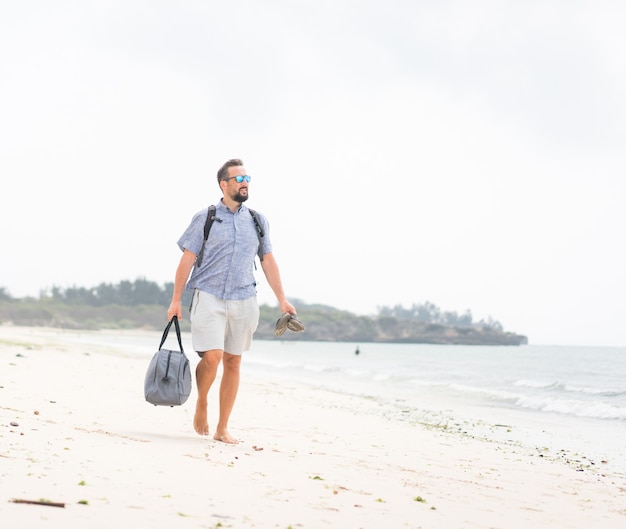 Homme adulte gai avec sac s'amuser sur la plage tropicale