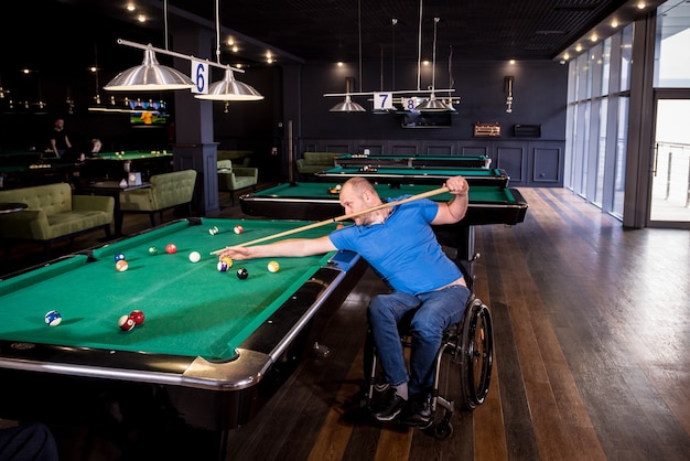 Un homme adulte handicapé en fauteuil roulant joue au billard dans le club