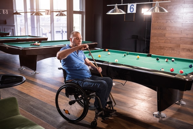 Un homme adulte handicapé en fauteuil roulant joue au billard dans le club