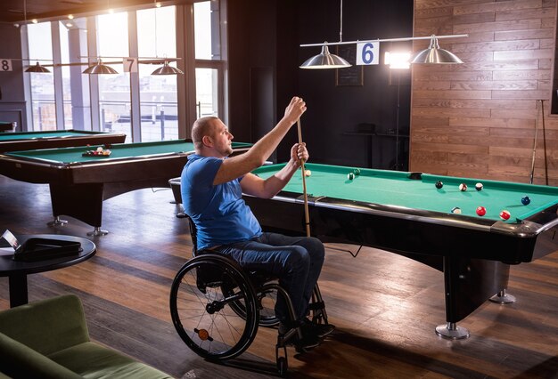 Un homme adulte handicapé en fauteuil roulant joue au billard dans le club