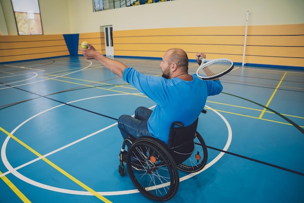 Homme adulte handicapé physique dans un fauteuil roulant jouant au tennis sur un court de tennis intérieur