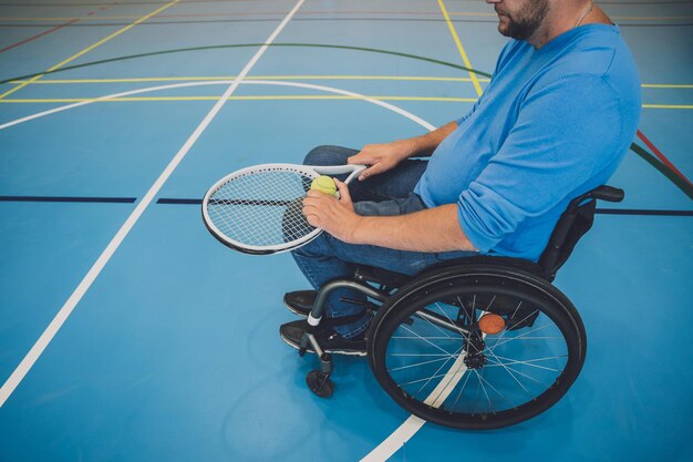Homme adulte handicapé physique qui utilise un fauteuil roulant pour jouer au tennis sur un court de tennis intérieur