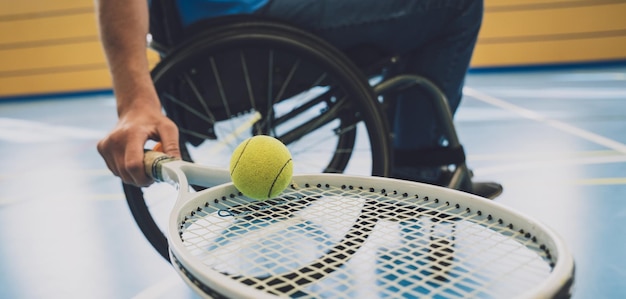 Homme adulte handicapé physique qui utilise un fauteuil roulant pour jouer au tennis sur un court de tennis intérieur