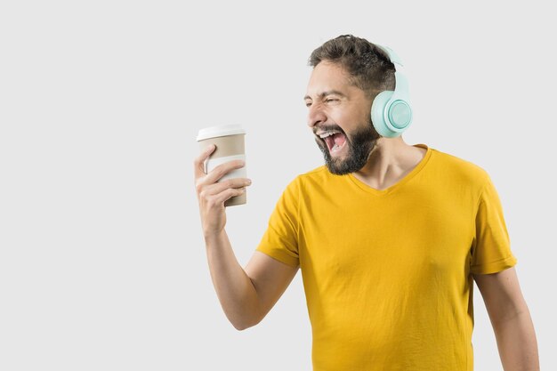 Un homme adulte latin avec une chemise jaune sur fond blanc chante pendant qu'il regarde sa tasse de café