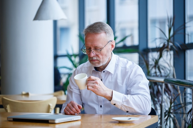 Homme adulte à lunettes manager businessman a travaillé avec succès et à la fin de la journée boit du café sans veste