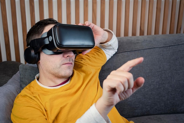 Un homme adulte mature souriant portant des lunettes VR appuie par son doigt sur l'interface de réalité virtuelle à la maison de la technologie de jeu métaverse visionnant une vidéo 360