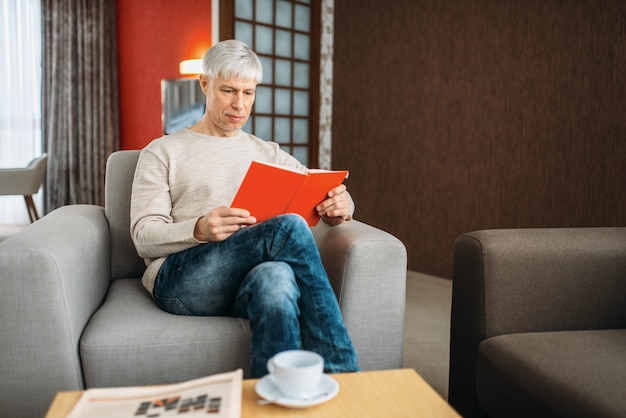 Homme adulte avec ordinateur portable assis sur un canapé à la maison. Personne de sexe masculin mature en jeans se détendre dans un fauteuil