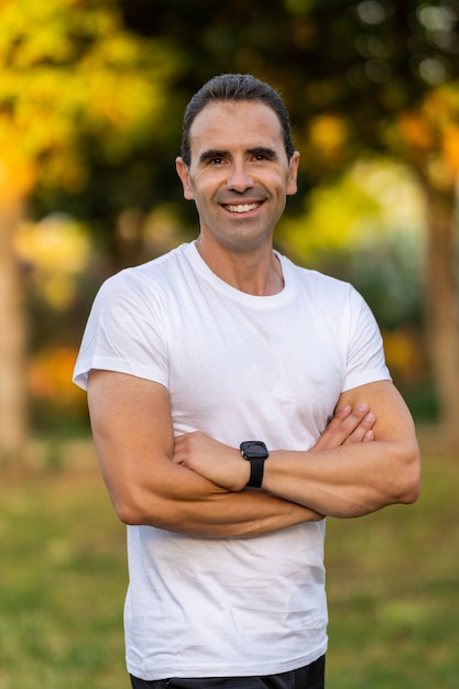 Homme adulte portant des vêtements de sport blancs croisant les bras et regardant la caméra. Il est souriant.
