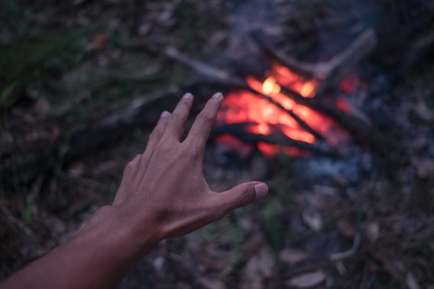 L&#39;homme adulte réchauffe les mains autour du feu de camp en forêt.