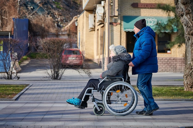 Un homme adulte roule sa mère handicapée sur des relations prudentes en fauteuil roulant avec une personne handicapée