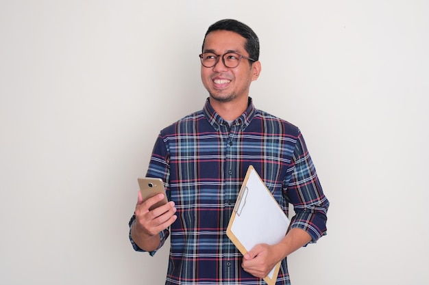 Photo un homme adulte souriant avec confiance tout en tenant un téléphone portable et un document en papier