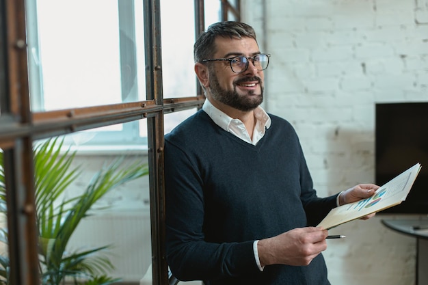 Homme adulte souriant portant des lunettes et tenant des papiers au bureau