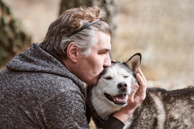 Homme adulte en sweat-shirt gris câlins et bisous chien Husky sibérien véritable amour de l'homme et de l'animal