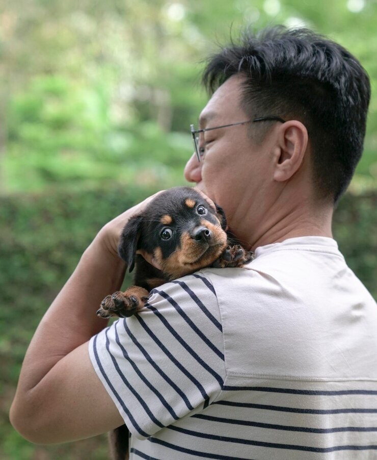 Homme adulte tenant un petit chiot sur son épaule
