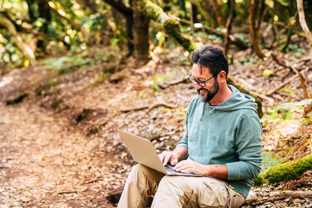 Un homme adulte travaille avec un ordinateur portable au milieu de la forêt sauvage verte