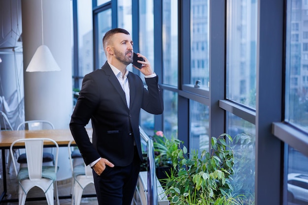 Homme d'affaires adulte, enseignant, mentor regarde par la grande fenêtre de son bureau. Travailler au bureau. Développement d'un nouveau projet d'entreprise