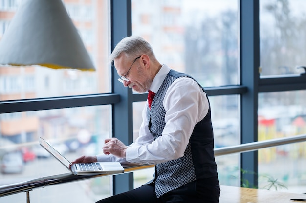 Homme d'affaires adulte, enseignant, mentor travaillant sur un nouveau projet. Assis près d'une grande fenêtre sur la table. Il regarde l'écran de l'ordinateur portable.