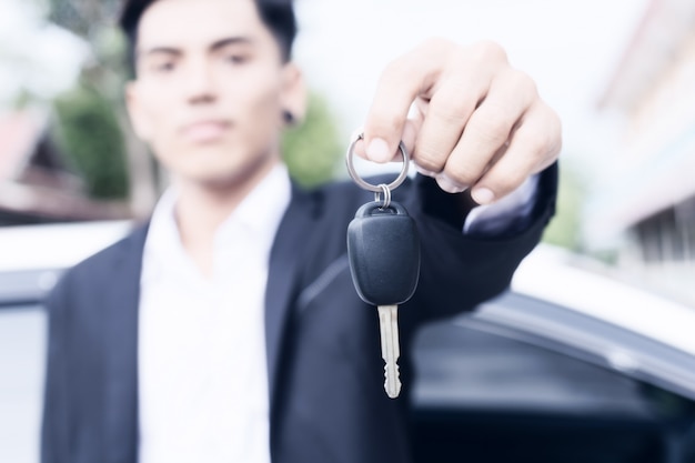 Homme d&#39;affaires adulte mâle en costume et tenant une clé de voiture à la main. Voitures blanches à l&#39;arrière-plan