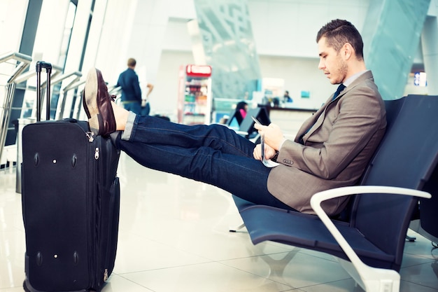 Photo homme d'affaires à l'aéroport avec un smartphone et une valise vérifiant ses e-mails avant d'embarquer