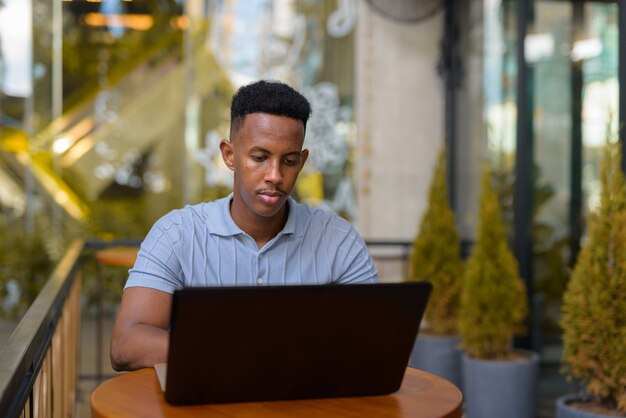 Homme d'affaires africain assis au café tout en utilisant un ordinateur portable