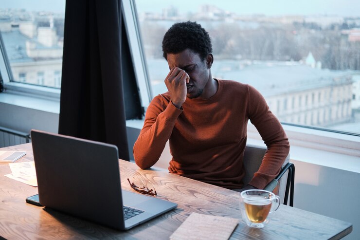 Photo homme d'affaires africain assis à la table devant un ordinateur portable et ayant l'air très fatigué