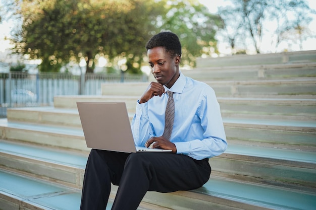 Homme d'affaires africain concentré travaillant avec son ordinateur portable Il est assis dans les escaliers